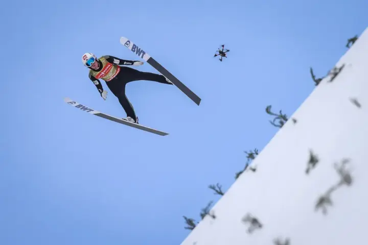 Skoczek narciarski w locie, z dronem w tle. Zastanawiasz się, ile waży skoczek narciarski, by osiągnąć taką odległość?