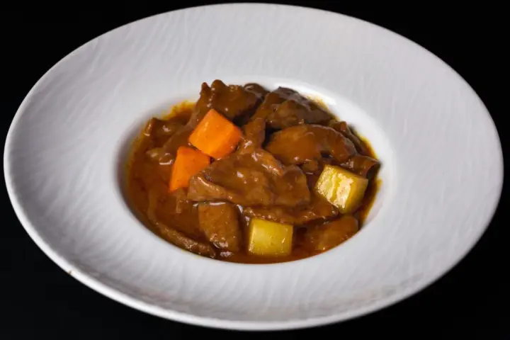 Un delicioso estofado de ternera con trozos de zanahoria y patata en una salsa espesa y aromática, servido en un plato blanco.