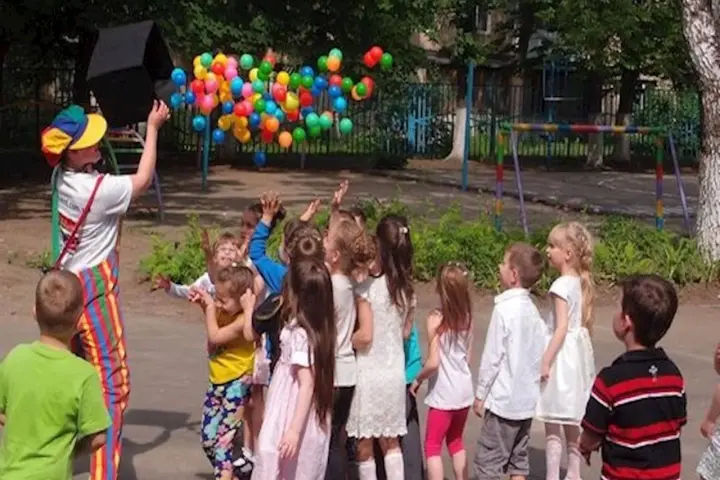 Klaun wypuszcza balony dla dzieci. Czy są zerówki w szkołach? Dzieci cieszą się zabawą na świeżym powietrzu.