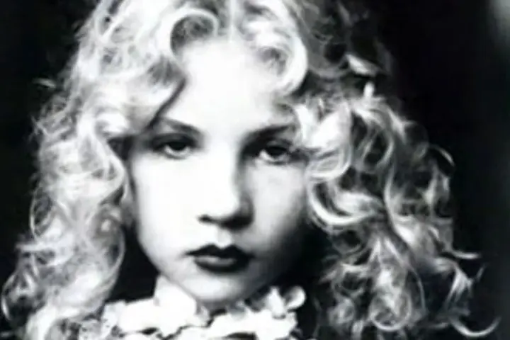 Portrait en noir et blanc d'Eva Ionesco enfant, aux boucles blondes et au regard intense.