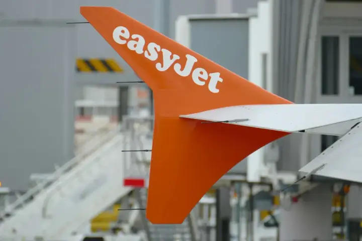 Pomarańczowy statecznik pionowy samolotu easyJet z białym logo, gotowy do przyjęcia bagażu pasażerów.