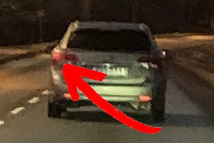 En röd pil pekar på bakljuset på en bil. Det är mörkt ute, och man undrar om man måste ha bakljus på dagen.