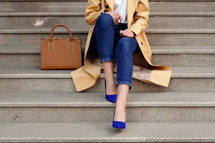 Elegancka stylizacja: beżowy płaszcz, jeansy i buty w kolorze habrowym. Obok torebka w odcieniu karmelu.