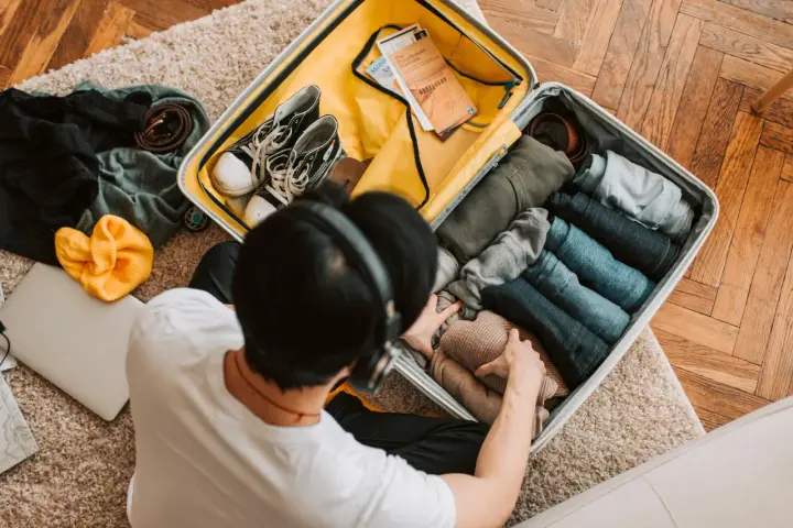 Preparazione per il mare: una valigia piena di vestiti piegati, scarpe, una felpa gialla e un laptop. Ecco cosa portare in vacanza al mare!
