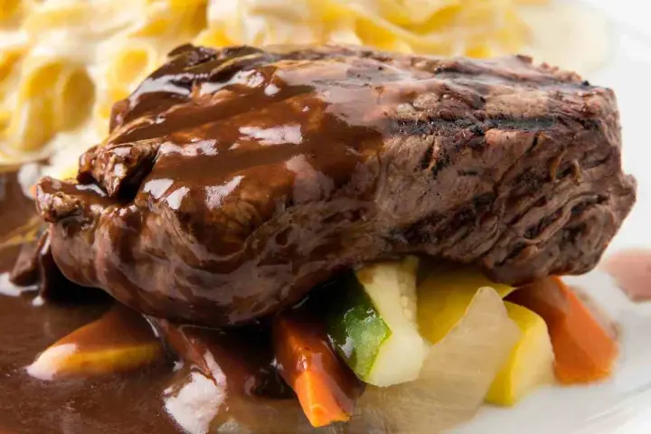 Succulento brasato di manzo nappato con salsa scura, servito su verdure miste e accompagnato da pasta.