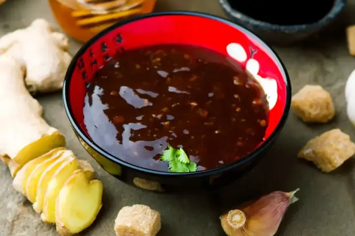 Miseczka z aromatycznym sosem teriyaki, obok świeży imbir, czosnek i brązowy cukier.