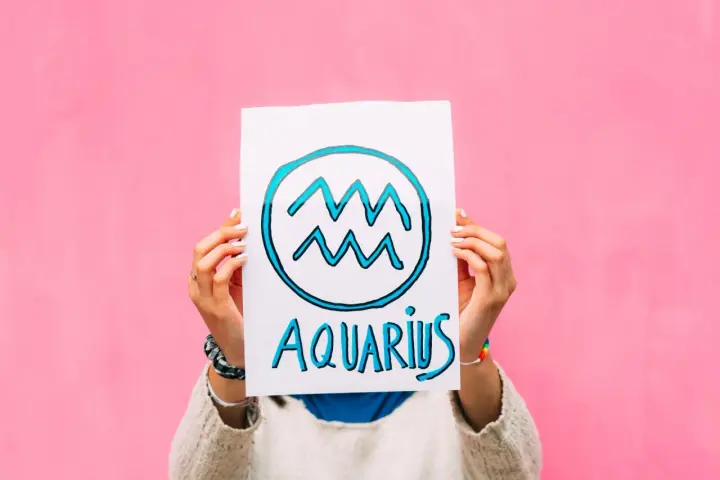 Waga i Wodnik: przyjaźń w kolorach tęczy. Ręce trzymają plakat z symbolem Wodnika i napisem "Aquarius" na różowym tle.