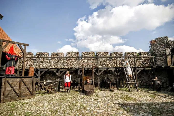 Scena z Muzeum Tortur w Krakowie: gilotyna, postacie w strojach historycznych i kamienne mury.