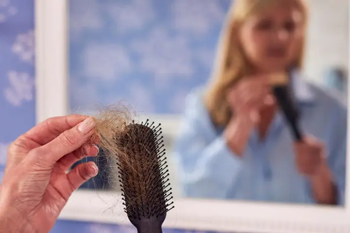 Frauen mit Haarausfall halten eine Bürste mit vielen Haaren. Im Spiegel sieht man eine Frau, die sich die Haare kämmt.
