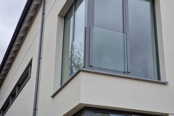 Nowoczesne portfenetry z przeszklonymi balustradami na jasnej elewacji.
