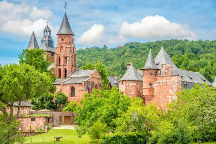 Magnifique ensemble de bâtiments en pierre rouge, dont une église romane et des tours, au milieu d'une végétation luxuriante. Idéal pour découvrir que faire autour de Rocamadour.