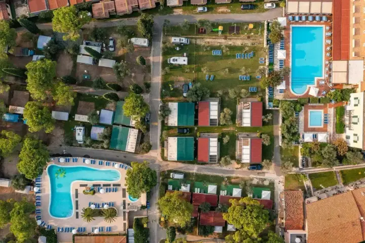 Widok z lotu ptaka na camping Toscolano: domki, baseny, przyczepy kempingowe i zielone tereny.