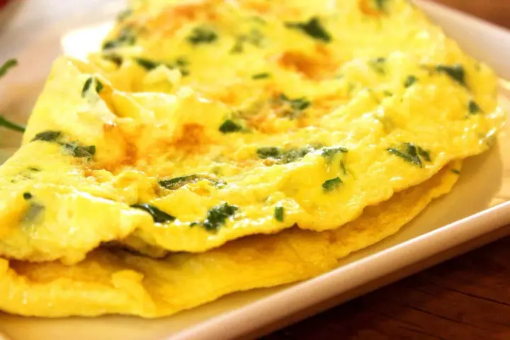 Złożony omlet z zielonymi ziołami na białym talerzu.