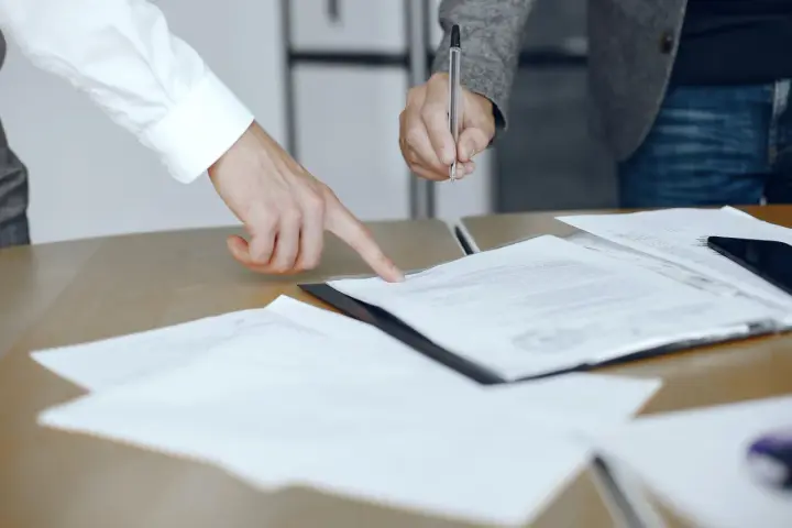 Dwie osoby przy biurku analizują dokumenty. Jedna wskazuje palcem na tekst, druga trzyma długopis, gotowa do podpisania. To może być moment, gdy omawiają, co to jest list żelazny.