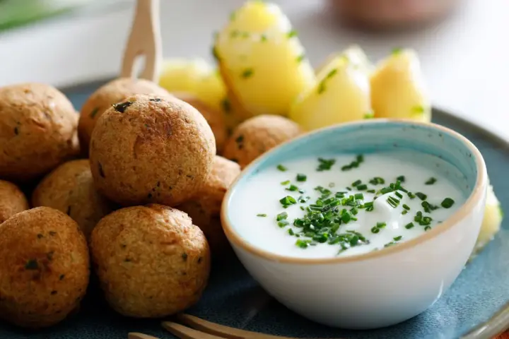 Polpette di ceci dorate e croccanti, servite con patate novelle e una ciotola di salsa cremosa guarnita con erba cipollina.