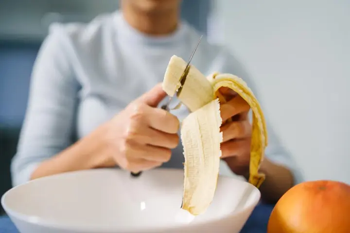 Une personne coupe une banane, riche en potassium, pour prendre soin de son cœur.