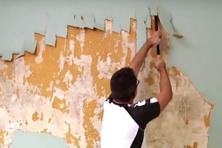 Man scraping old wallpaper off a wall.