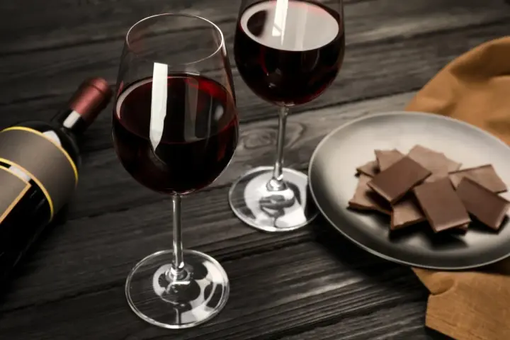 Deux verres de vin rouge, une bouteille et une assiette de chocolat, prêts pour un accord vin chocolat parfait.