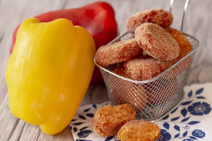 Polpette di peperoni dorate e croccanti, servite in un cestino, accanto a peperoni freschi rossi e gialli.