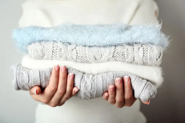 Pile de pulls en laine douce, gris et blanc, avec un pull bleu ciel. Idéal pour savoir comment detacher un pull blanc et le garder comme neuf.