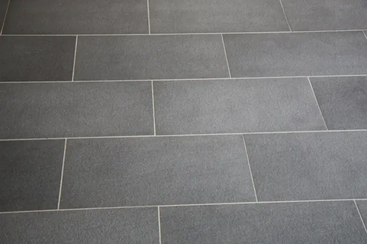 Détail d'un sol en carrelage gris anthracite, avec un joint carrelage couleur crème qui souligne la pose rectiligne.