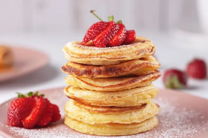 Pancakes dorati, perfetti per una ricetta pancake veloce senza lievito, guarniti con fragole fresche e zucchero a velo.