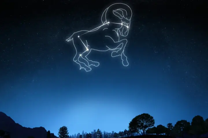 Gwiazdozbiór Barana na tle nocnego nieba. Widać jego sylwetkę z charakterystycznymi rogami, jakby unosił się nad ciemnym krajobrazem gór i drzew.