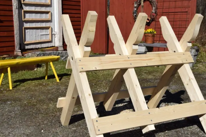 Nybyggd sågbock i trä, redo för att bygga ved. En gul bänk syns i bakgrunden.