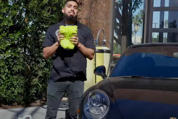 Man holding a fluffy wash mitt, ready to demonstrate how to wash a convertible car.