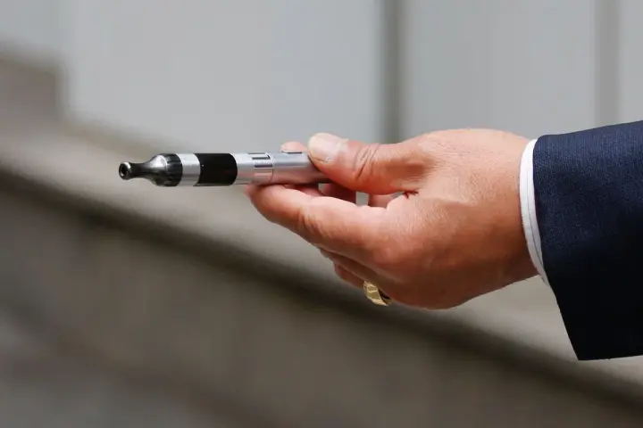 Mano con traje sosteniendo un cigarrillo electrónico, listo para vapear en el trabajo.