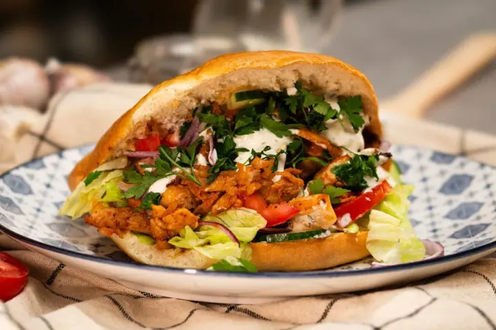 Pyszny, domowy kebab z kurczaka z piekarnika, pełen świeżych warzyw i sosu, na ozdobnym talerzu.