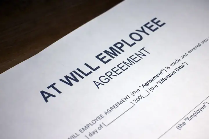 Close-up of an "At Will Employee Agreement" document, illustrating what does at-will employment mean: either party can terminate the relationship at any time.
