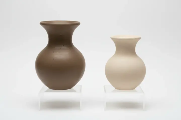Två vaser, en i mörkbrun och en i ljusbeige, som om de vore formade av blå lera.