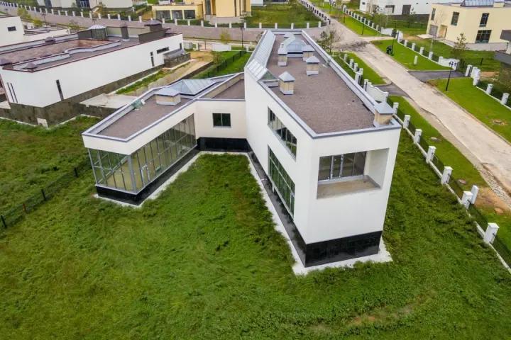 Casa moderna con grandes ventanales y tejado plano, rodeada de césped. Se puede poner una casa prefabricada en un terreno urbano como esta.