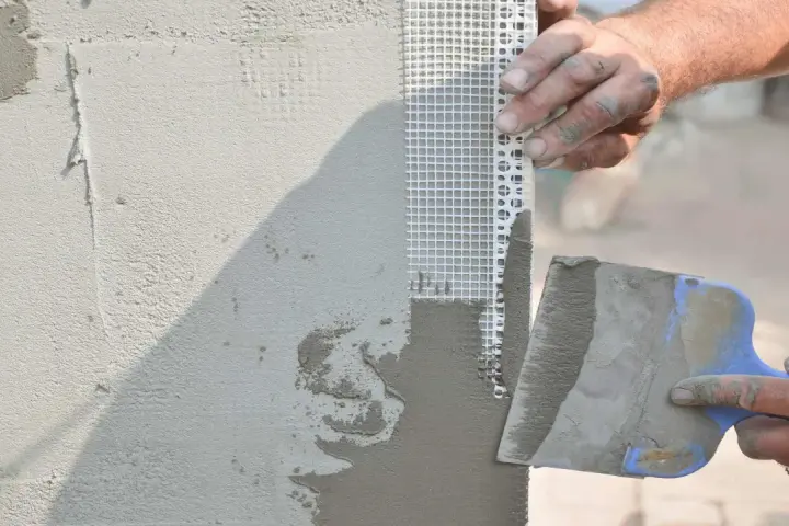 Mani esperte applicano stucco e rete per stuccare angolo muro, garantendo una finitura perfetta.