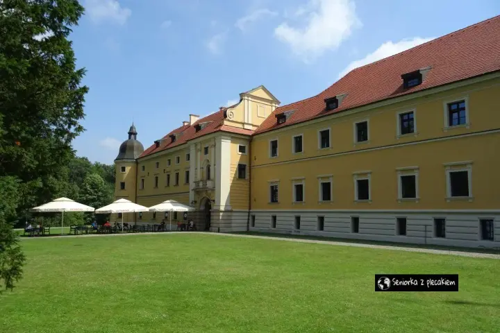 Żółty budynek opactwa cystersów w Rudach z czerwonym dachem i zielonym trawnikiem przed nim.