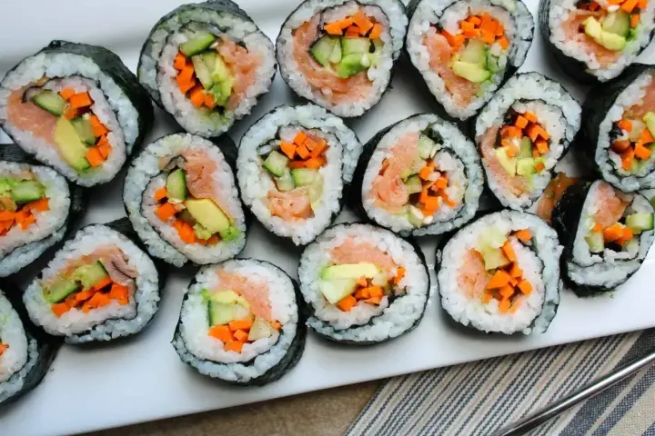 Ułożone na talerzu rolki sushi z łososiem, awokado, ogórkiem i marchewką. Widać, co do sushi do środka, czyli świeże składniki.