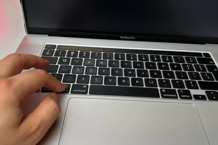Dłoń naciska klawisz "command" na klawiaturze MacBooka, przygotowując się do instalacji drukarki.