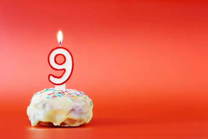 En söt donut med vit glasyr och strössel, toppad med en brinnande ljusformad siffra nio. Perfekt för ett kalas för en 9-årig kille!