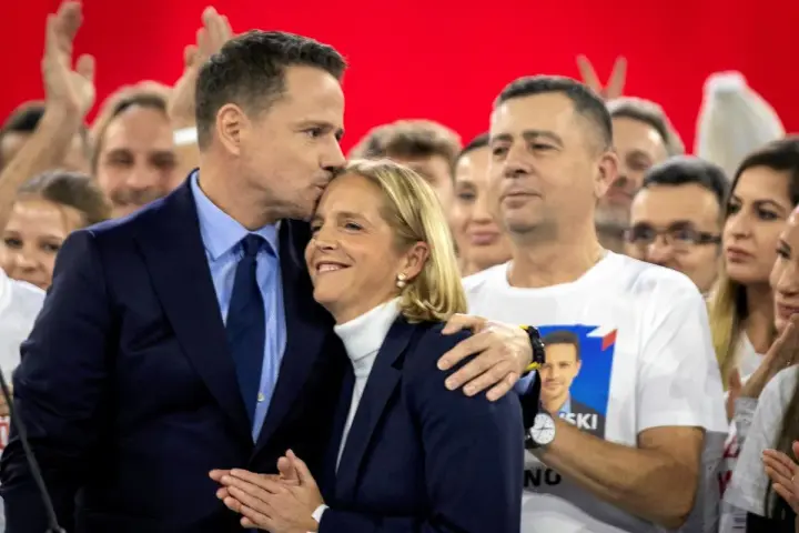 Rafał Trzaskowski, choć nie znamy jego dokładnego wieku, czule całuje żonę na tle tłumu.