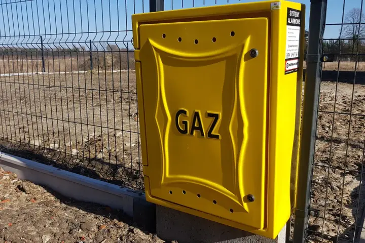 Żółta skrzynka gazowa z napisem "GAZ" przy ogrodzeniu. Zastanawiasz się, ile kosztuje przyłącze gazu?