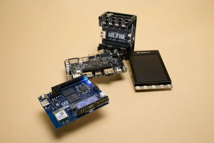 An Arduino Uno, a Bela GEN MULTI, and a Fruit Jam RP2350 board are arranged on a beige surface, showcasing some of the best microcontroller options for makers.