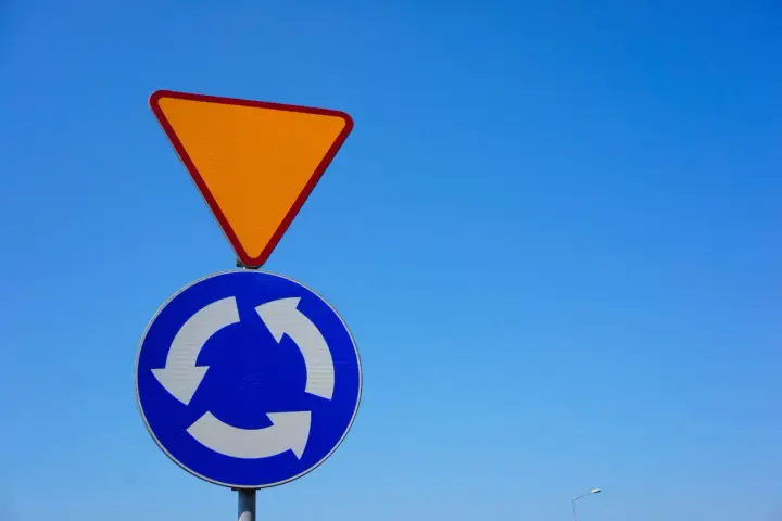 Znak ustąp pierwszeństwa i znak informujący o ruchu okrężnym na tle błękitnego nieba.