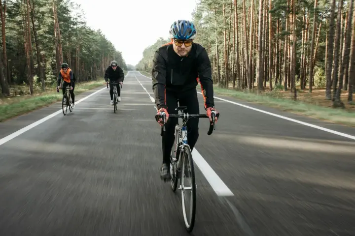 Cyclists on a road through a forest, likely engaged in a VO2 max training program, pushing their limits.