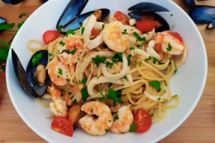 Pyszne linguini z krewetkami, kalmarami i małżami, ozdobione pomidorkami i natką pietruszki.