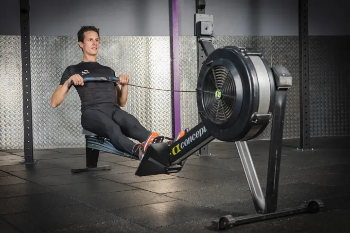 Un homme en tenue de sport effectue un exercice rameur dans une salle de sport.