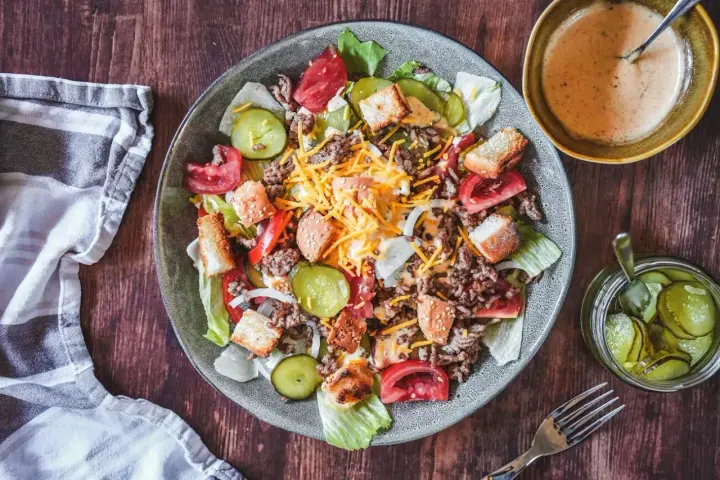 Ein Big Mac Salat mit Hackfleisch, Käse, Tomaten, Gurken und Croutons. Dazu eine cremige Sauce und eingelegte Gurken.