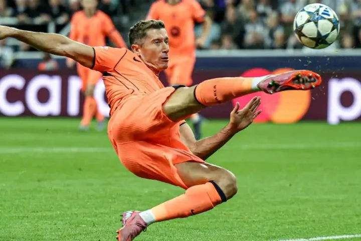 Piłkarz w pomarańczowym stroju wykonuje akrobatyczne kopnięcie do piłki. To Robert Lewandowski, który gra w Lidze Mistrzów.