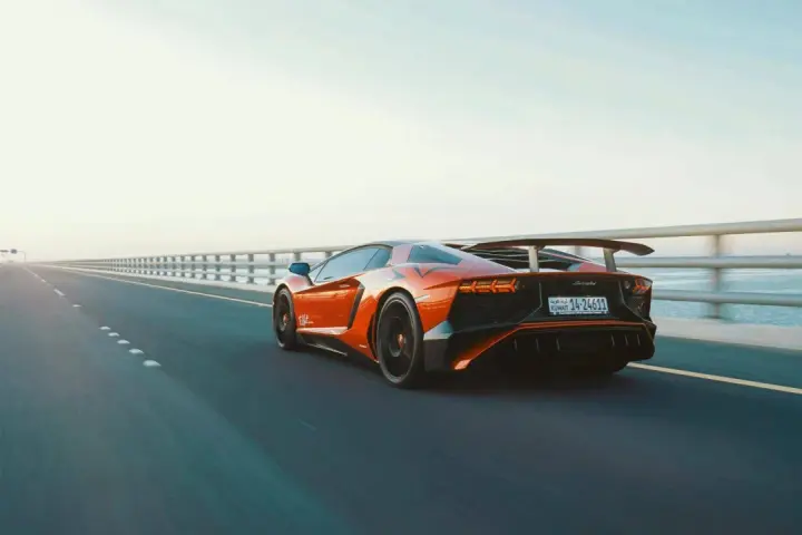 Arancia Lamborghini sfreccia su un ponte, i suoi cavalli scatenati sull'asfalto. L'auto sportiva domina la scena, un'icona di velocità.