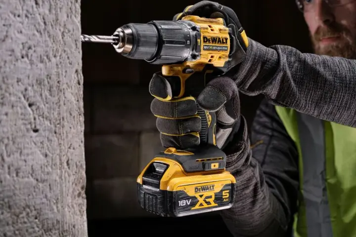 Mężczyzna w rękawicach wierci w betonie najmocniejszą wkrętarką DeWalt 18V XR.